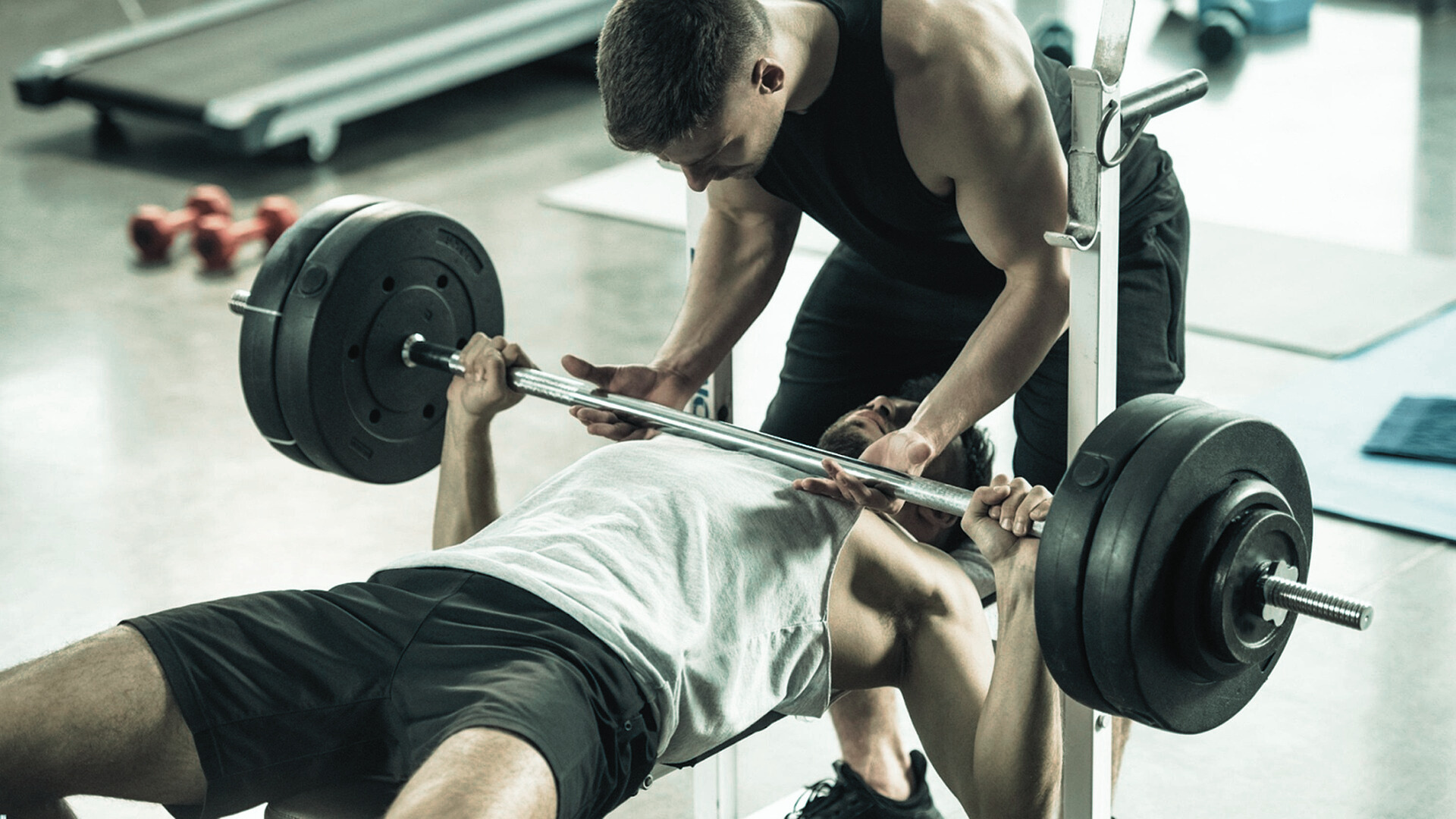Man performing a heavy bench press with a spotter assisting during a strength training workout