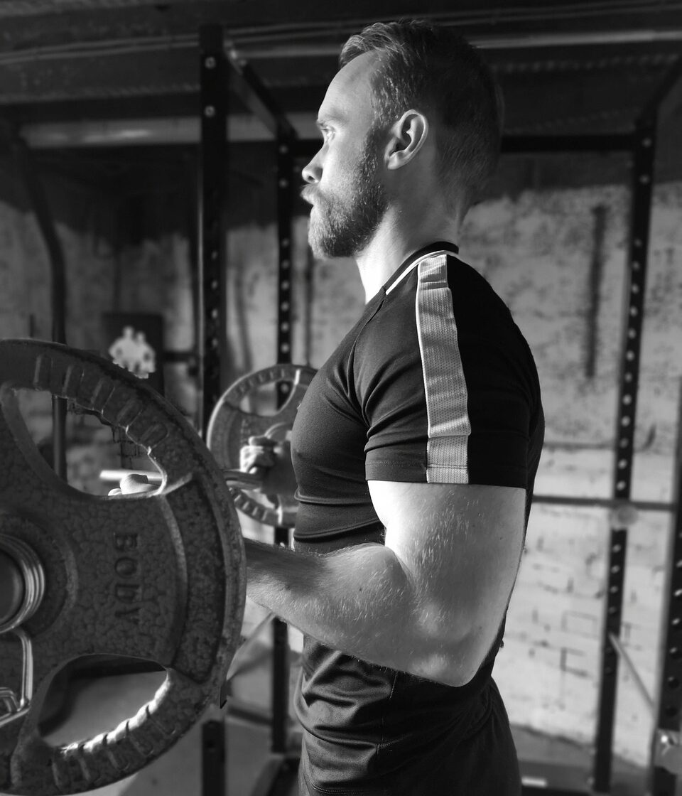 Man performing standing barbell curls in a gym with proper form